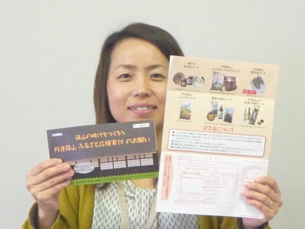 担当の女性職員が「ふるさと応援寄付のお願い」のパンフレットと返礼品の写真と振込用紙が一緒になった用紙を持っている写真